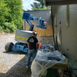 Worker operating a blue boom lift near a building's exterior wall.