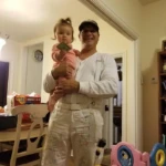 A man in white holding a young child in a cozy living room.