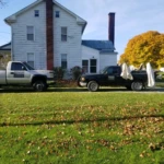 Two trucks parked beside a white house on a sunny day.