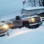 Two trucks parked in a snowy driveway with an American flag in the background.