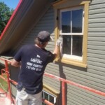 Worker painting window trim on a house exterior.